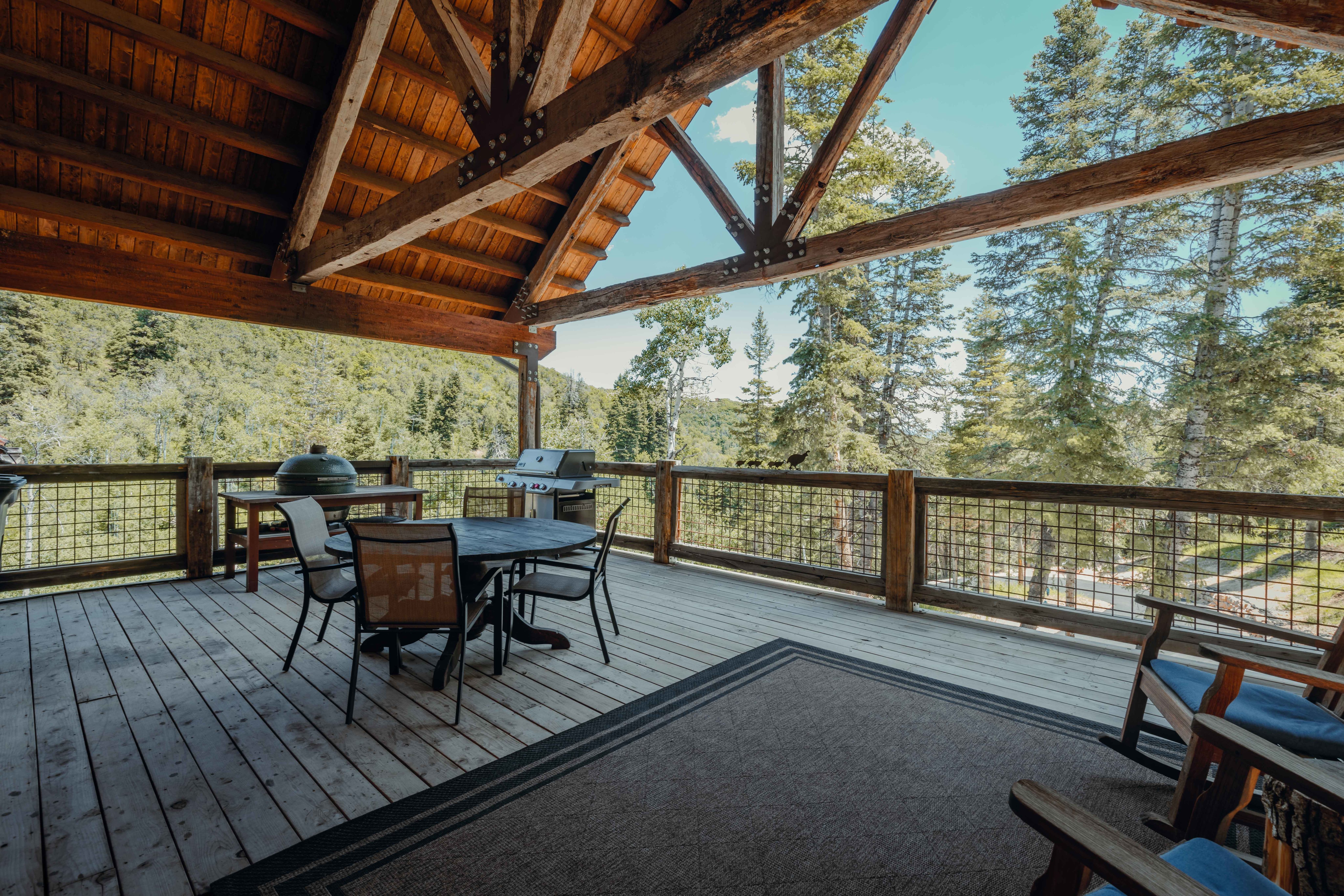 Expansive covered deck featuring a natural wood ceiling with exposed beams, wood-finish decking, and a metal grid railing