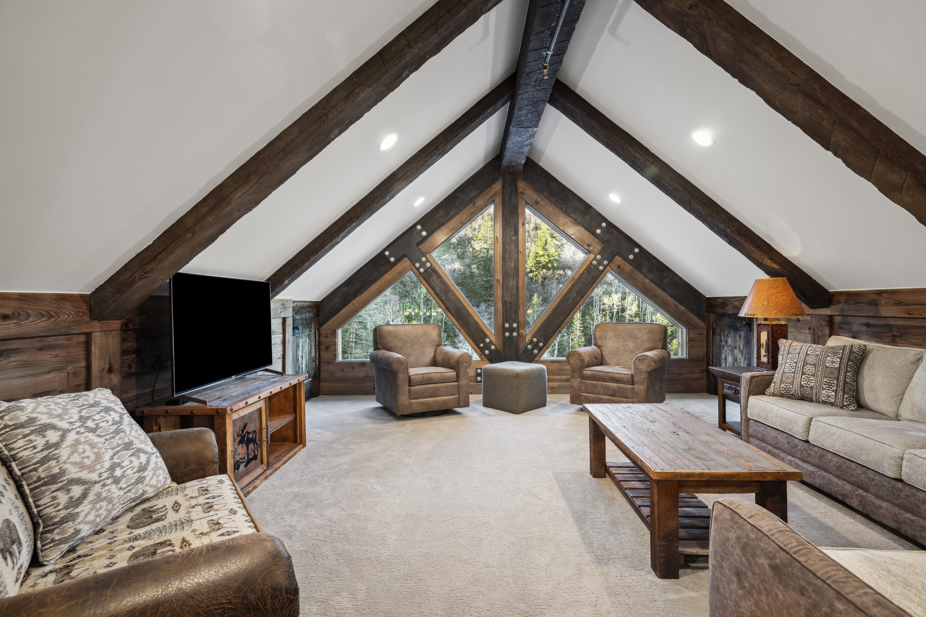 Vaulted ceilings with exposed wood beams, expansive triangular windows, recessed lighting, and wood-paneled walls