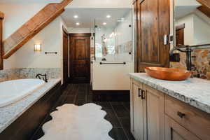 Bathroom featuring a full-size soaking tub with a stone-finish surround, a frameless glass shower enclosure, a vanity with a copper vessel sink and stone countertop, wood-finish flooring, and exposed ceiling beams