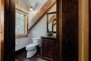 Powder room featuring a stone vessel sink, dark wood-finish vanity with an integrated mirror, and exposed wood beam accents
