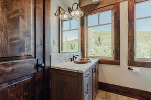 Bathroom vanity featuring a vessel sink, stone countertop, wood-finish cabinetry, and framed mirror