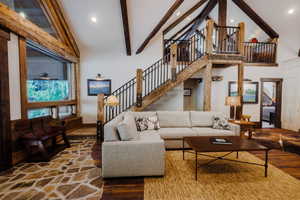 Vaulted ceiling with exposed wood beams, a prominent staircase with iron railings, flagstone flooring, and large windows
