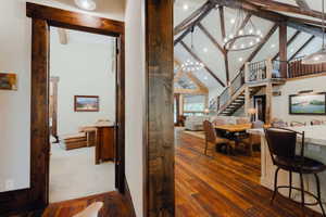 Spacious living area featuring exposed wood beams, vaulted ceilings, wood-finish flooring, a contemporary chandelier, and a prominent staircase with metal railings