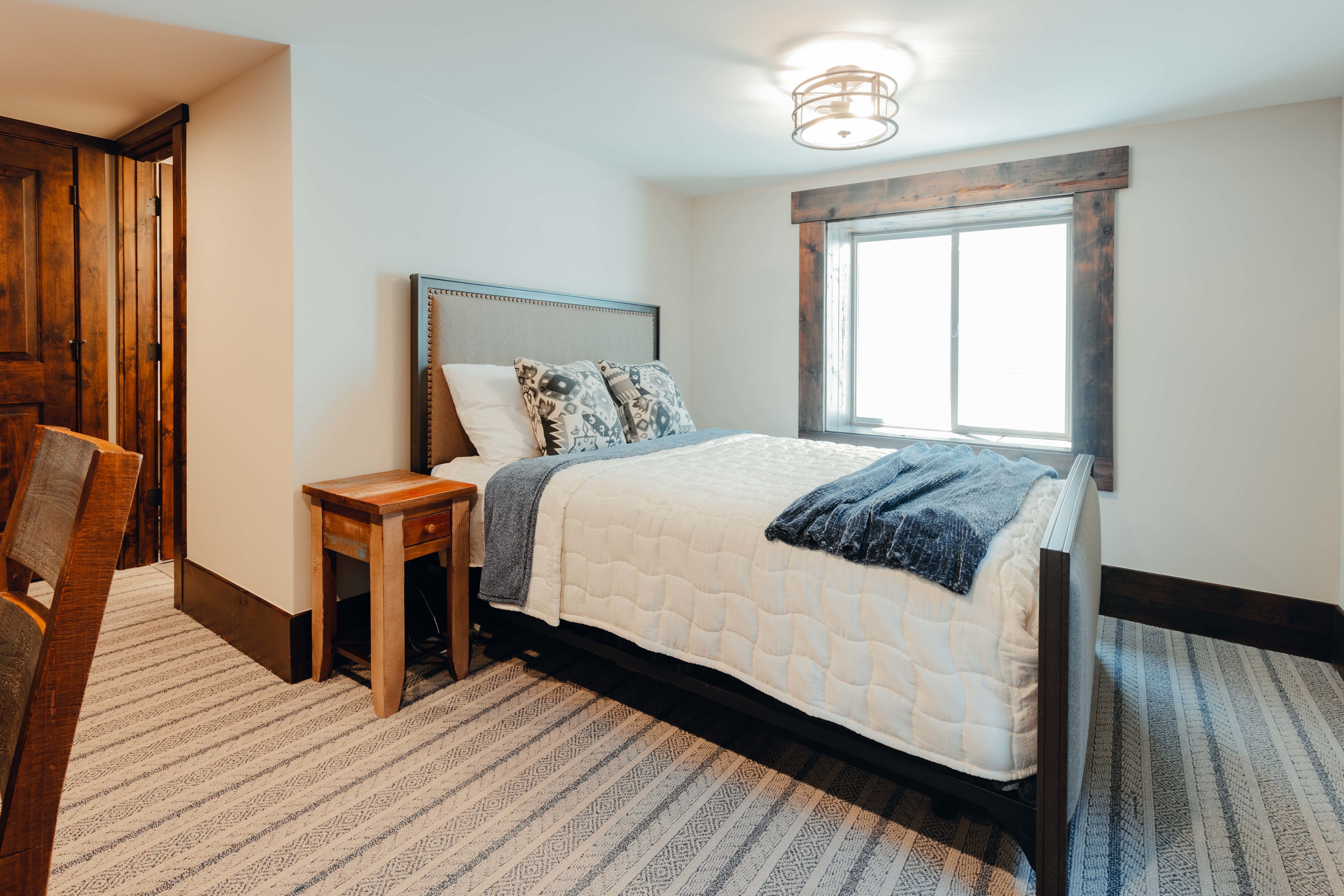 Bedroom featuring a window with rustic wood trim, a contemporary ceiling fixture, and patterned carpet flooring