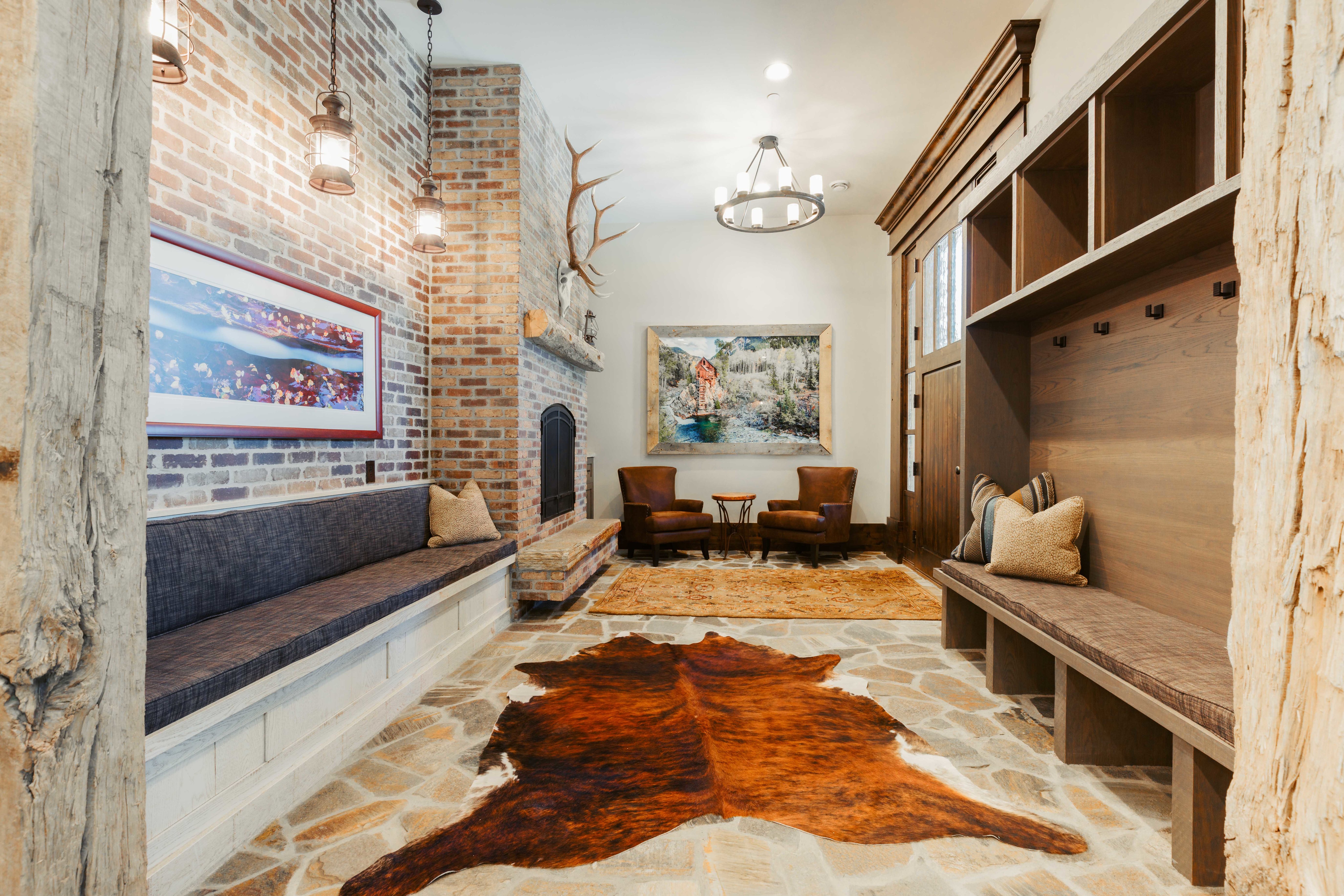 Spacious mudroom featuring flagstone flooring, a large brick fireplace, built-in bench seating, and an integrated wood-finish storage system with cubbies and hooks