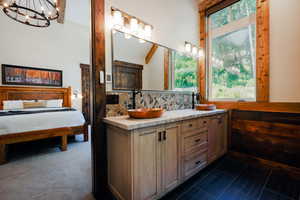 Double vanity featuring copper vessel sinks, matte black fixtures, stone tile backsplash, and a light-toned countertop