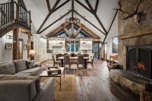 Vaulted ceiling with exposed wood beams, stone fireplace with a substantial hearth, wood-finish flooring, custom cabinetry in the kitchen, and a dining area with pendant lighting
