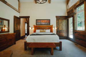 Spacious room featuring vaulted ceilings with exposed wood beams, warm wood-finish doors and trim, full-height windows, and wall-mounted sconces