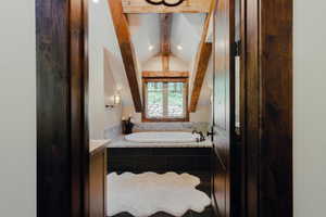 Attic bathroom featuring exposed wood beams, a built-in soaking tub with a dark tile surround, a wood-framed window, recessed lighting, and sconce lighting