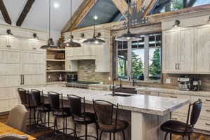 Expansive kitchen featuring a large island with countertop seating, stone countertops, a full-height brick backsplash, exposed wood beam ceiling, and multiple pendant light fixtures