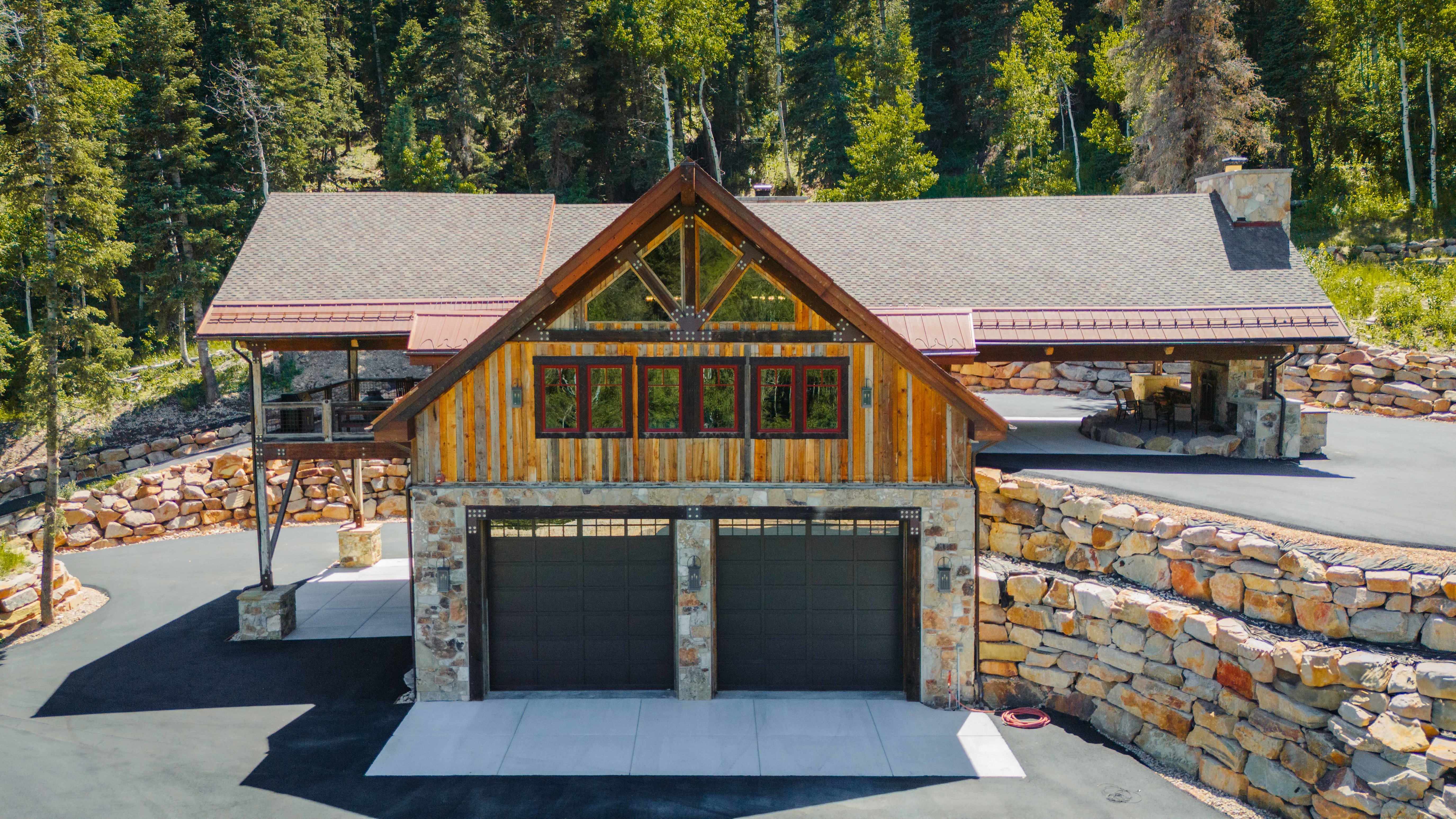 Rustic-modern exterior featuring stone and wood siding, a two-car garage, and a covered patio area with a stone fireplace