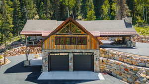 Rustic-modern exterior featuring stone and wood siding, a two-car garage, and a covered patio area with a stone fireplace