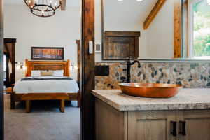Copper vessel sink with an oil-rubbed bronze faucet on a speckled countertop, complemented by a river rock backsplash and wood-finish cabinetry