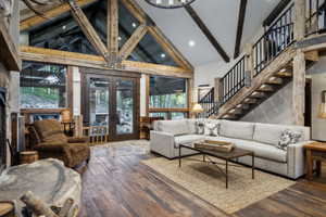 Vaulted ceiling with exposed wood beams and architectural glass, rich wood-finish flooring, stone fireplace, and a striking open staircase with iron railings