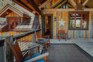 Expansive outdoor deck featuring wood-plank flooring, a wood and wire railing, and exposed ceiling beams