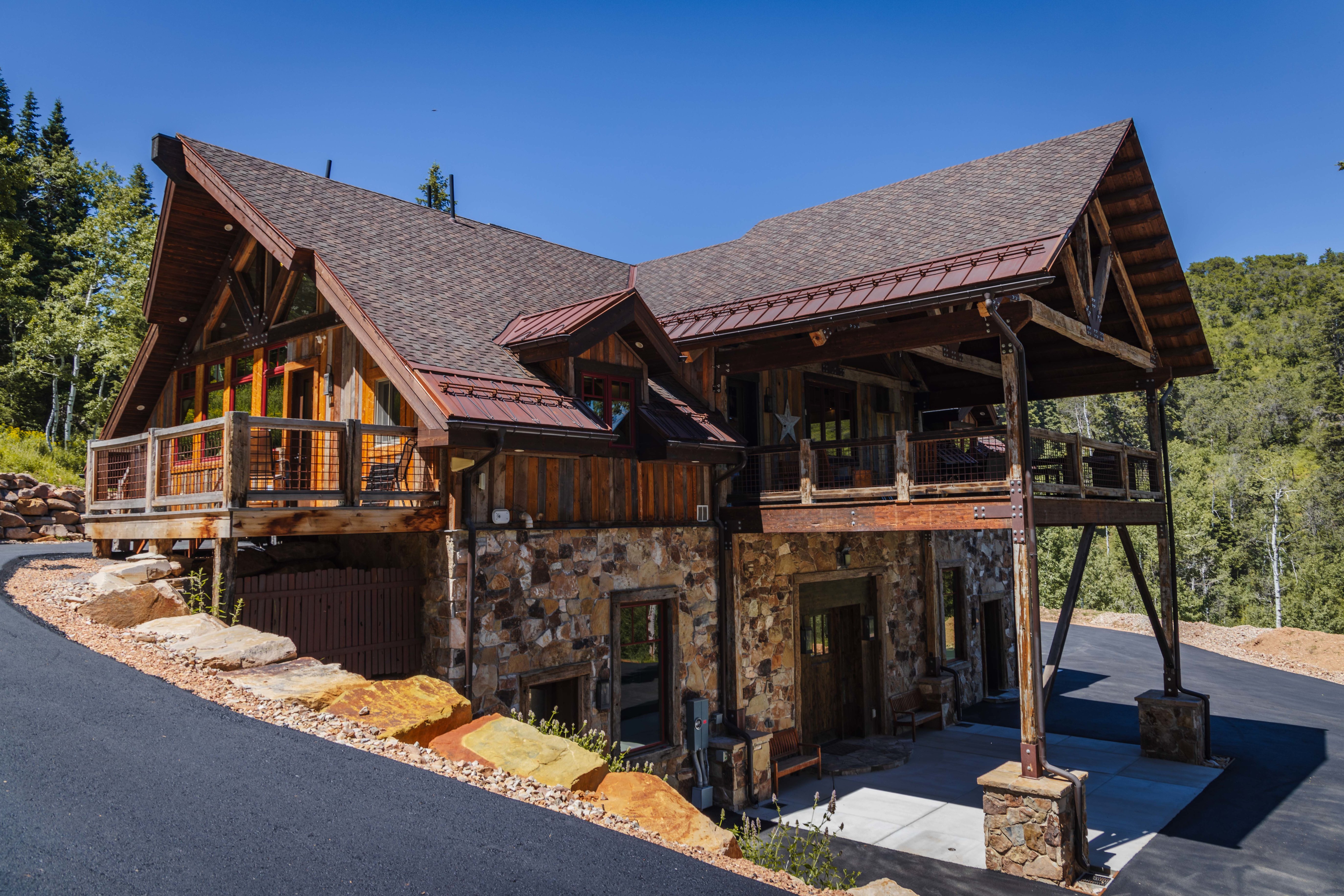 Rustic-modern residence featuring a stone and wood facade, a covered carport, and multiple balconies
