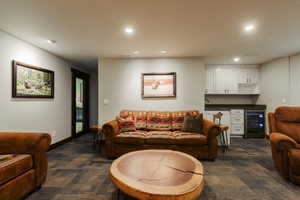 Recreation room featuring recessed lighting, patterned carpet flooring, a dark wood-framed doorway, and a built-in wet bar with white cabinetry, dark countertops, and a beverage refrigerator