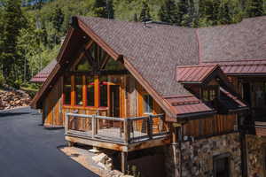 Rustic exterior featuring wood siding, a stone foundation, a composition shingle roof, and a red metal roof accent