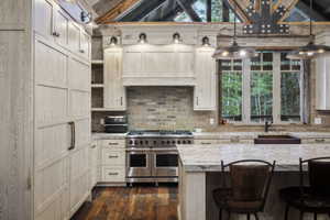 Gourmet kitchen featuring a professional-grade stainless steel range, light wood-finish cabinetry, stone countertops, a brick-patterned backsplash, and rich wood-finish flooring