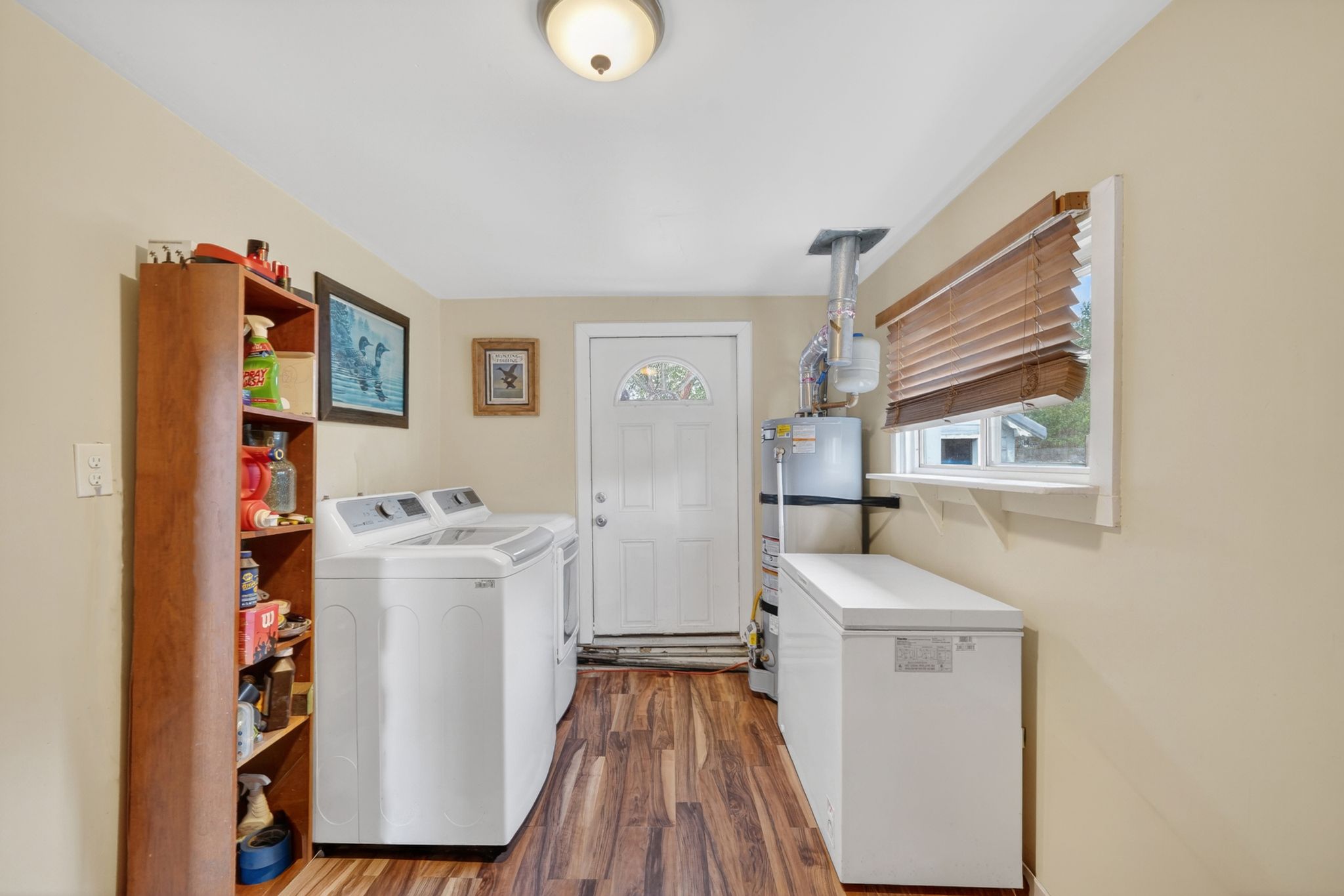 Dedicated utility space featuring wood-finish flooring, a rear exterior door with a decorative glass insert, and a window with horizontal blinds