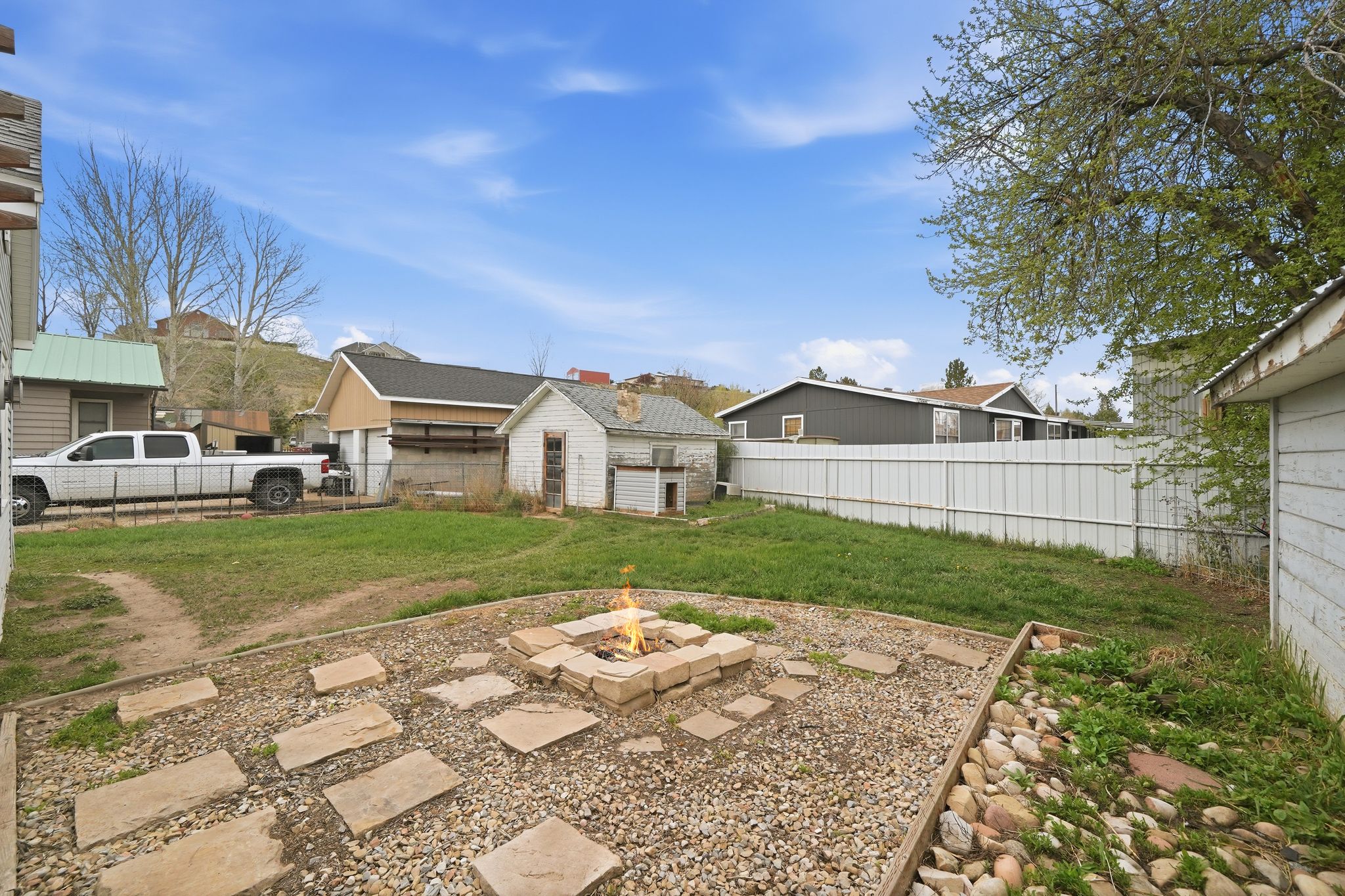 Expansive backyard featuring a central fire pit with stone pavers, a gravel patio area, and a separate storage shed