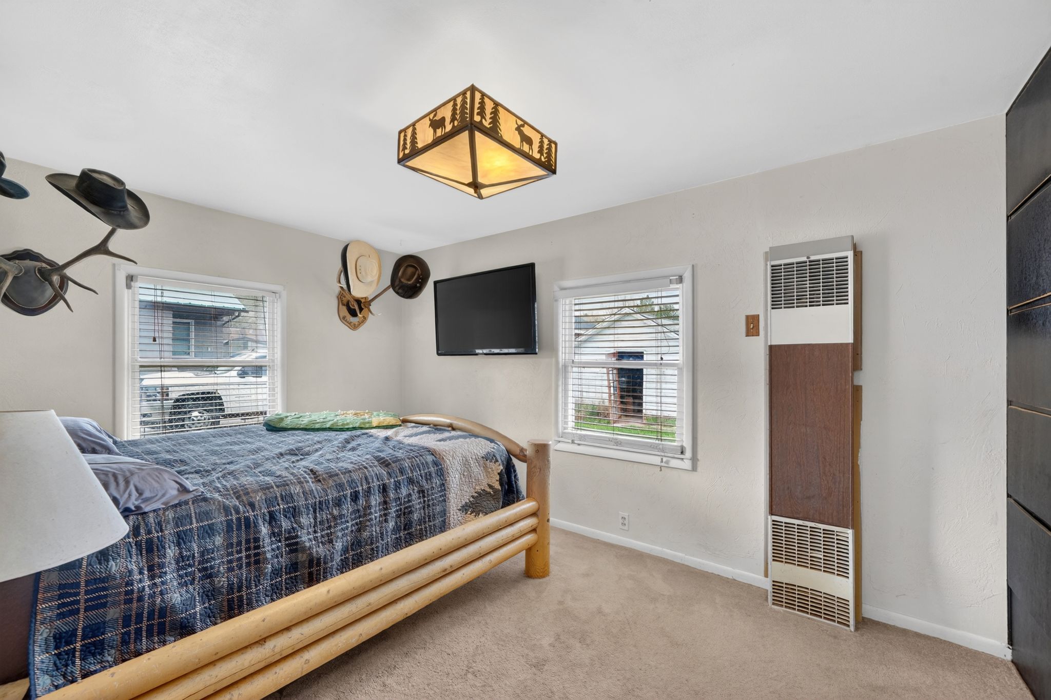 White walls with textured finish, light-colored carpet flooring, a decorative ceiling light fixture, and a wall-mounted heating unit with a wood-finish panel