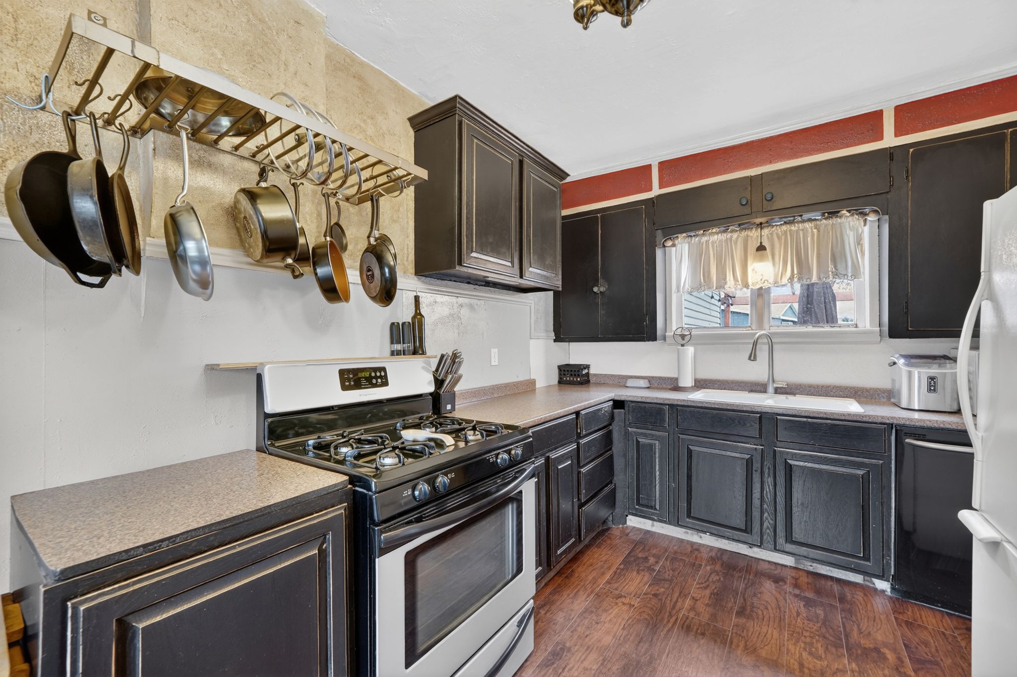 Kitchen featuring dark wood-finish cabinetry, stainless steel gas range, a white single-basin sink with a chrome faucet, wood-finish flooring, and light-toned countertops