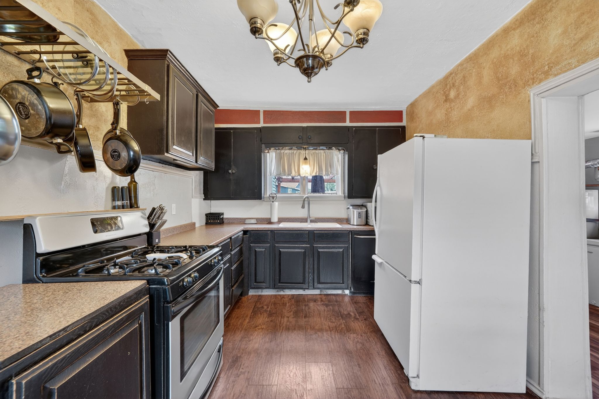 Galley kitchen featuring dark wood-finish cabinetry, a gas range, wood-finish flooring, and a ceiling-mounted chandelier