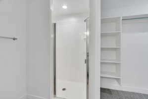 Walk-in shower with a chrome-framed glass door, recessed lighting, and a built-in shelving unit