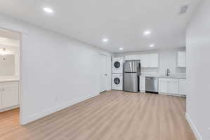 Open-concept living space featuring wood-finish flooring, recessed lighting, and a full kitchen with white cabinetry, stainless steel appliances, and a stacked washer and dryer