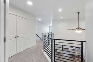 Upper-level landing featuring light gray carpeting, recessed ceiling lighting, a ceiling fan with integrated lighting, modern black horizontal bar railings, and white panel doors with arched tops