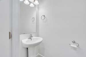 Pedestal sink with chrome faucet, wall-mounted mirror, and vanity lighting