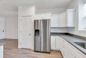 Kitchen featuring white cabinetry, stainless steel side-by-side refrigerator, gray countertops, and wood-finish flooring