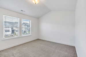 Carpeted interior space featuring a vaulted ceiling, two windows with blinds, a white ceiling fixture, white baseboards, and a white wall finish