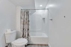 Bathroom featuring a white toilet, integrated shower and bathtub unit, wall-mounted towel bar, and recessed lighting