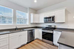 Kitchen featuring white cabinetry, grey countertops, stainless steel appliances, and wood-finish flooring