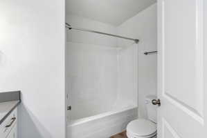 Bathroom featuring a white bathtub/shower combination with a chrome shower rod, a white toilet, and a vanity with a dark countertop and white cabinetry