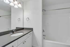Bathroom featuring a spacious vanity with an undermount sink, a large mirror, white cabinetry, a dark countertop, and a shower-tub combination