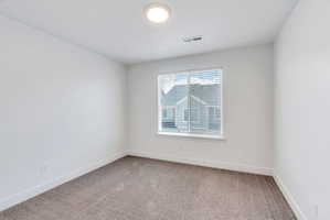 Bright room featuring a large window with blinds, neutral-toned carpet flooring, white walls, and a ceiling-mounted light fixture