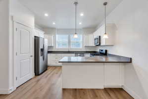Modern kitchen featuring wood-finish flooring, white cabinetry, dark countertops, a stainless steel refrigerator, and pendant lighting