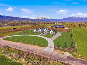 Expansive property featuring a contemporary residence with a circular driveway, substantial green lawns, and a distant mountainous backdrop