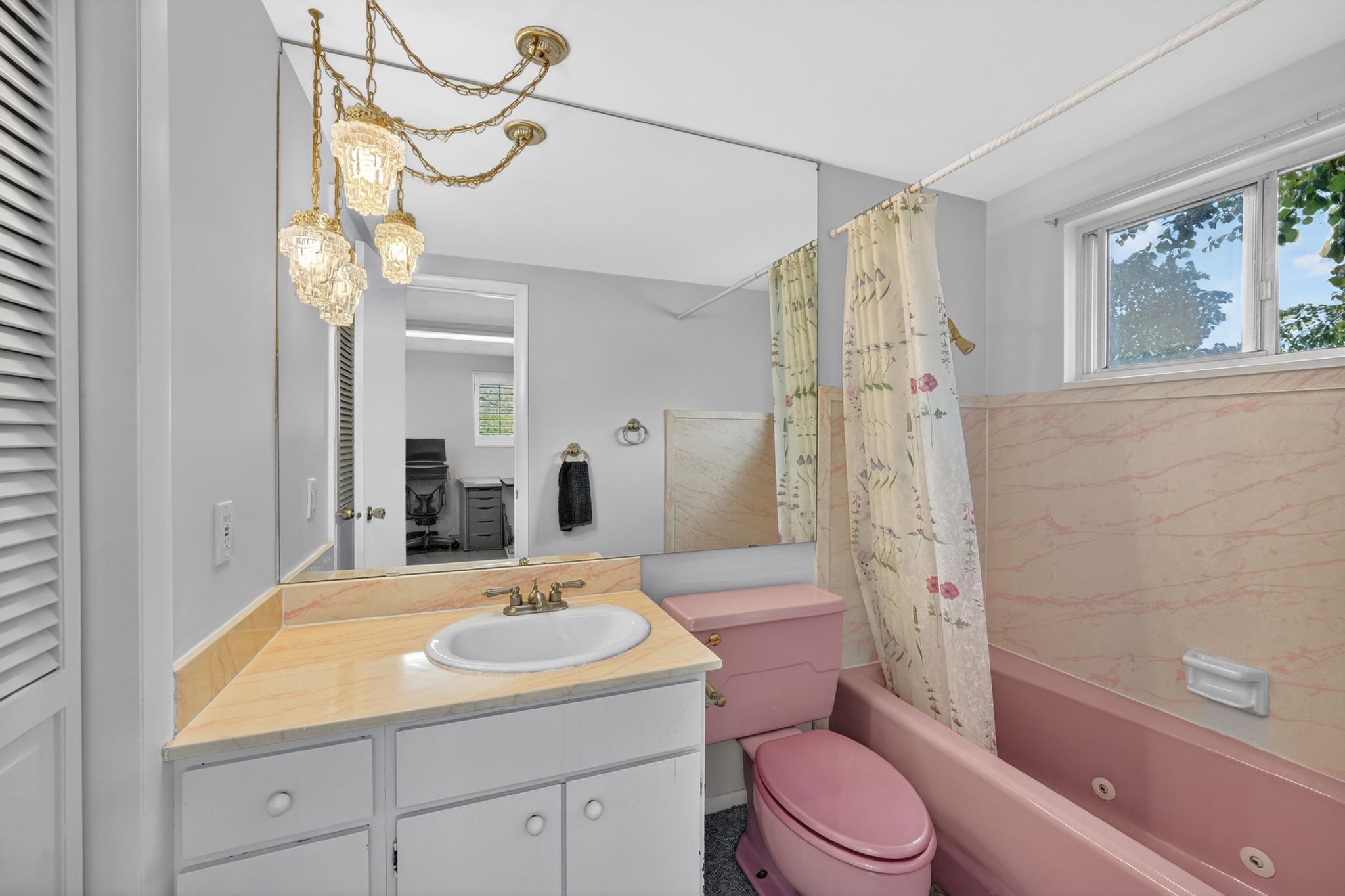 Bathroom featuring a pink tub and toilet, an integrated vanity sink, a full-wall mirror, and a multi-bulb chandelier