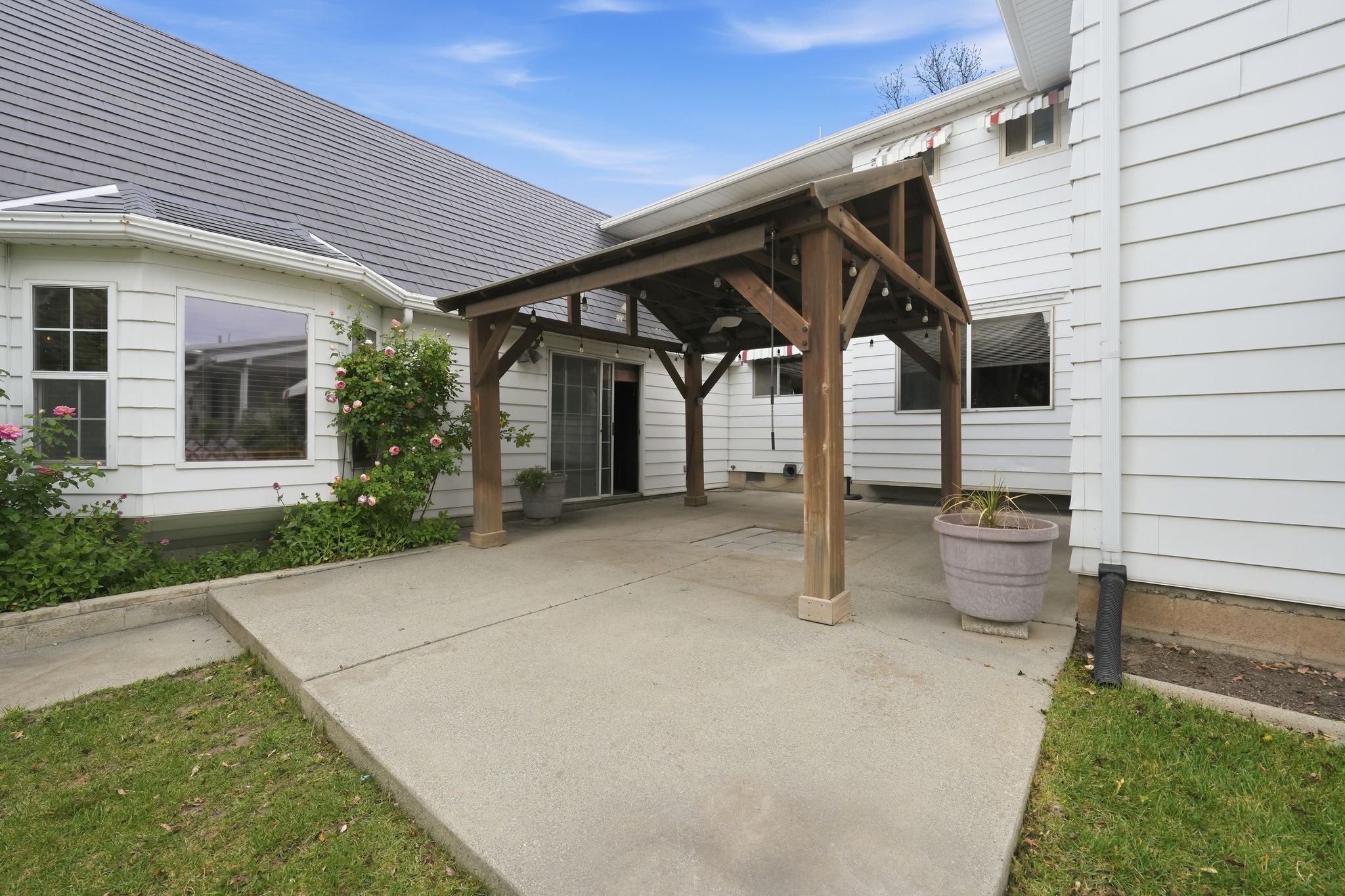 Covered patio with exposed wood beams, concrete flooring, and string lighting