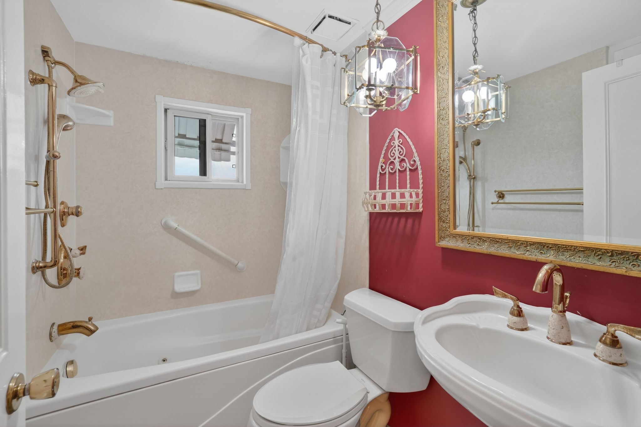 Full bathroom featuring a white tub, brass-finish shower fixtures, a sliding window, and a white pedestal sink with brass-finish hardware
