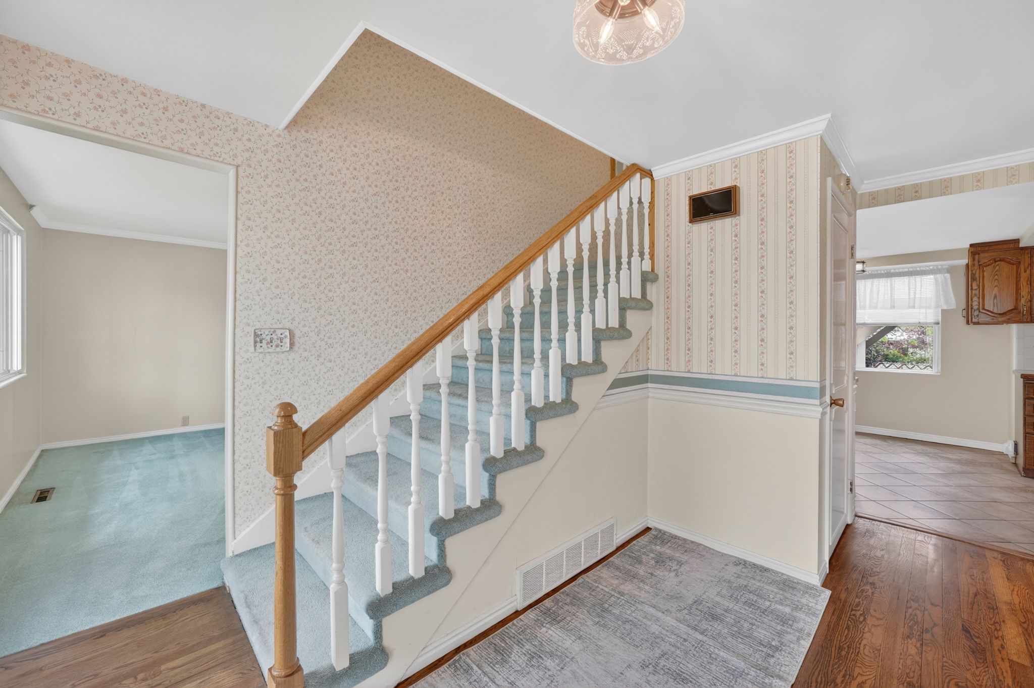 Hardwood flooring with a patterned area rug at the base of the staircase, featuring a wood handrail and white balusters