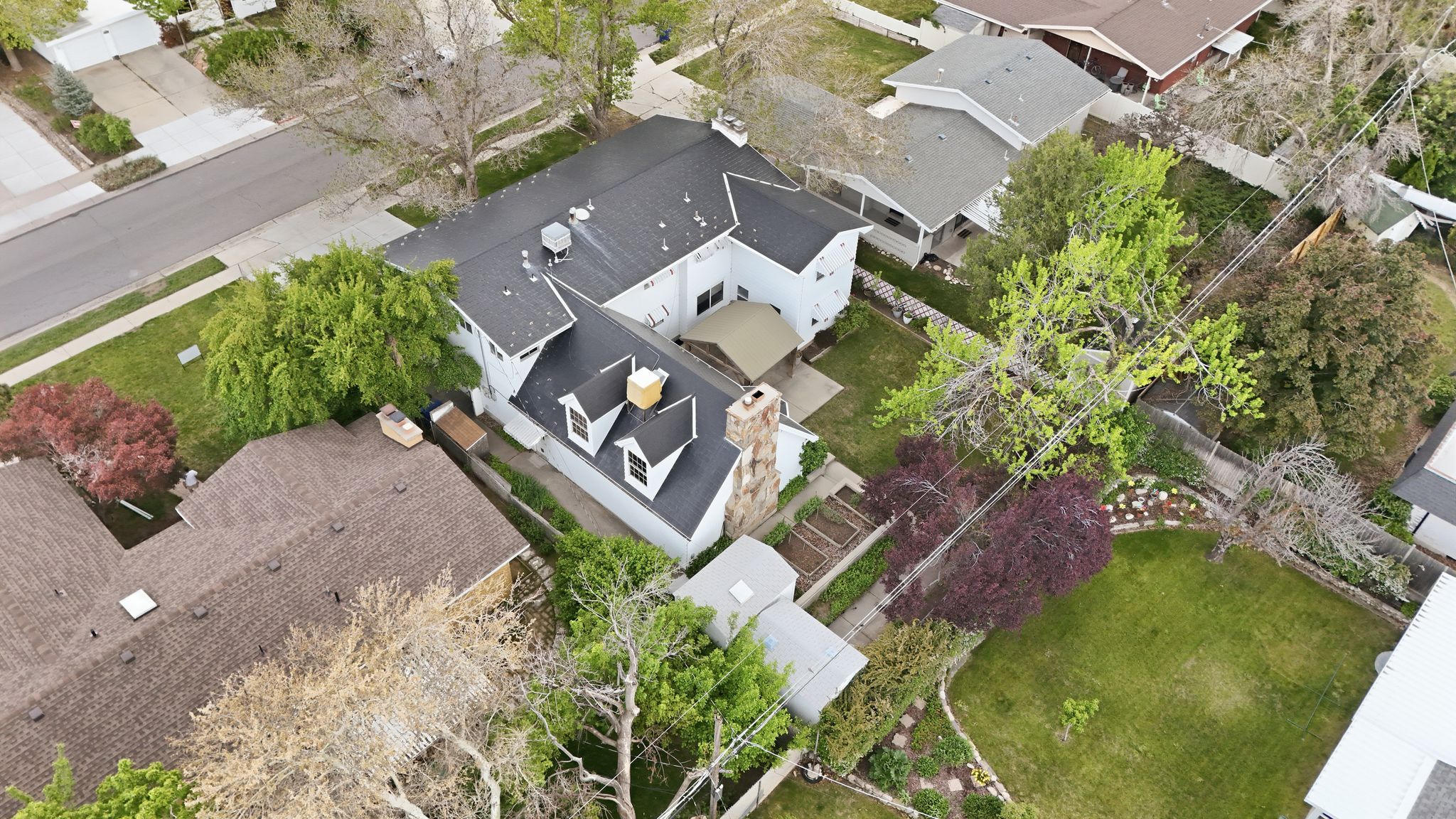 Aerial perspective showcasing the property with dark shingle roofing, multiple dormer windows, and a prominent stone chimney
