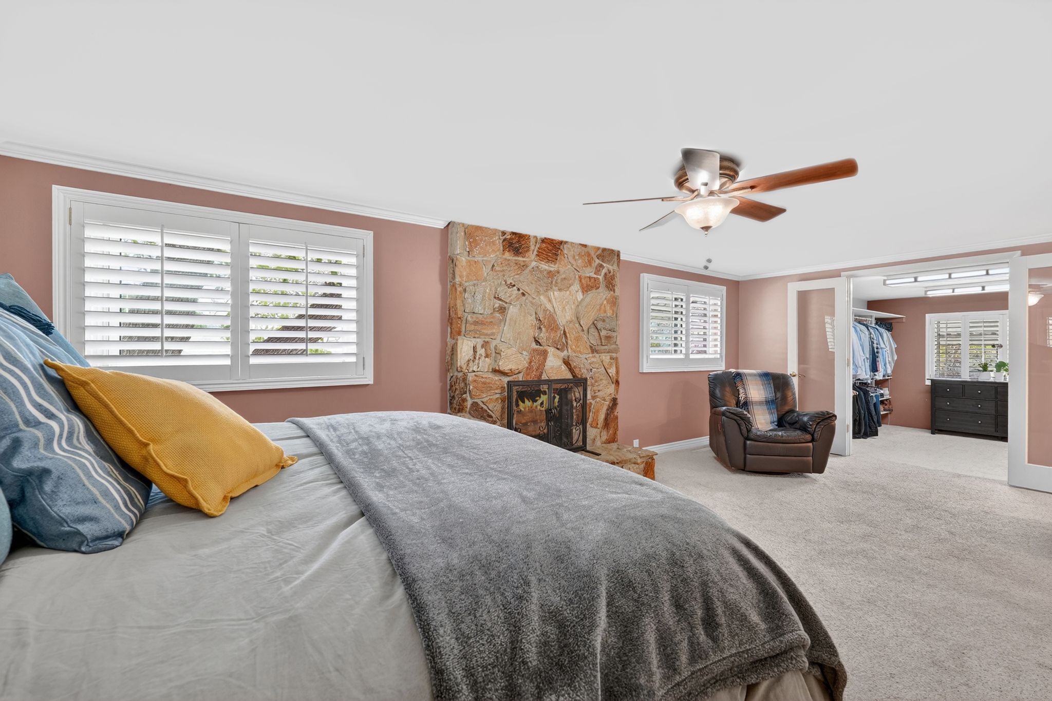 Spacious carpeted room featuring a stone-clad fireplace and multiple windows with plantation shutters