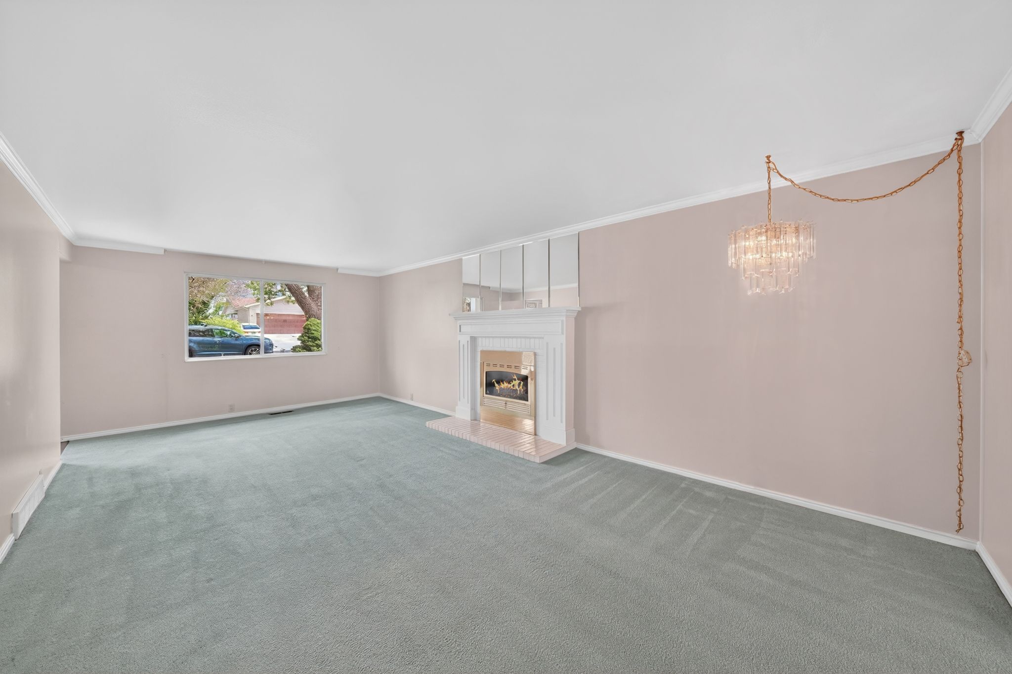 Spacious room featuring a fireplace with a white mantel and hearth, a crystal chandelier, crown molding, and light blue carpeting