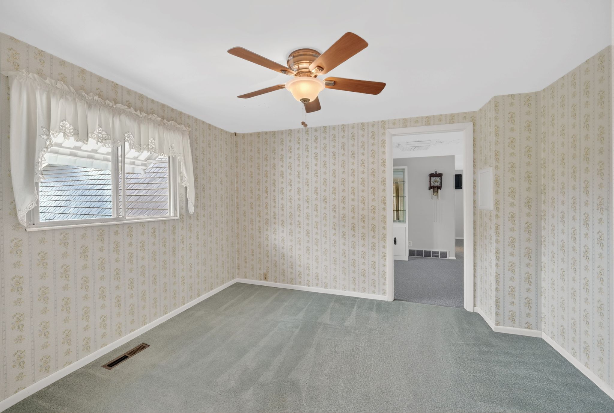 Room featuring patterned wallpaper, light blue carpeting, a ceiling fan with light fixture, and a window with blinds