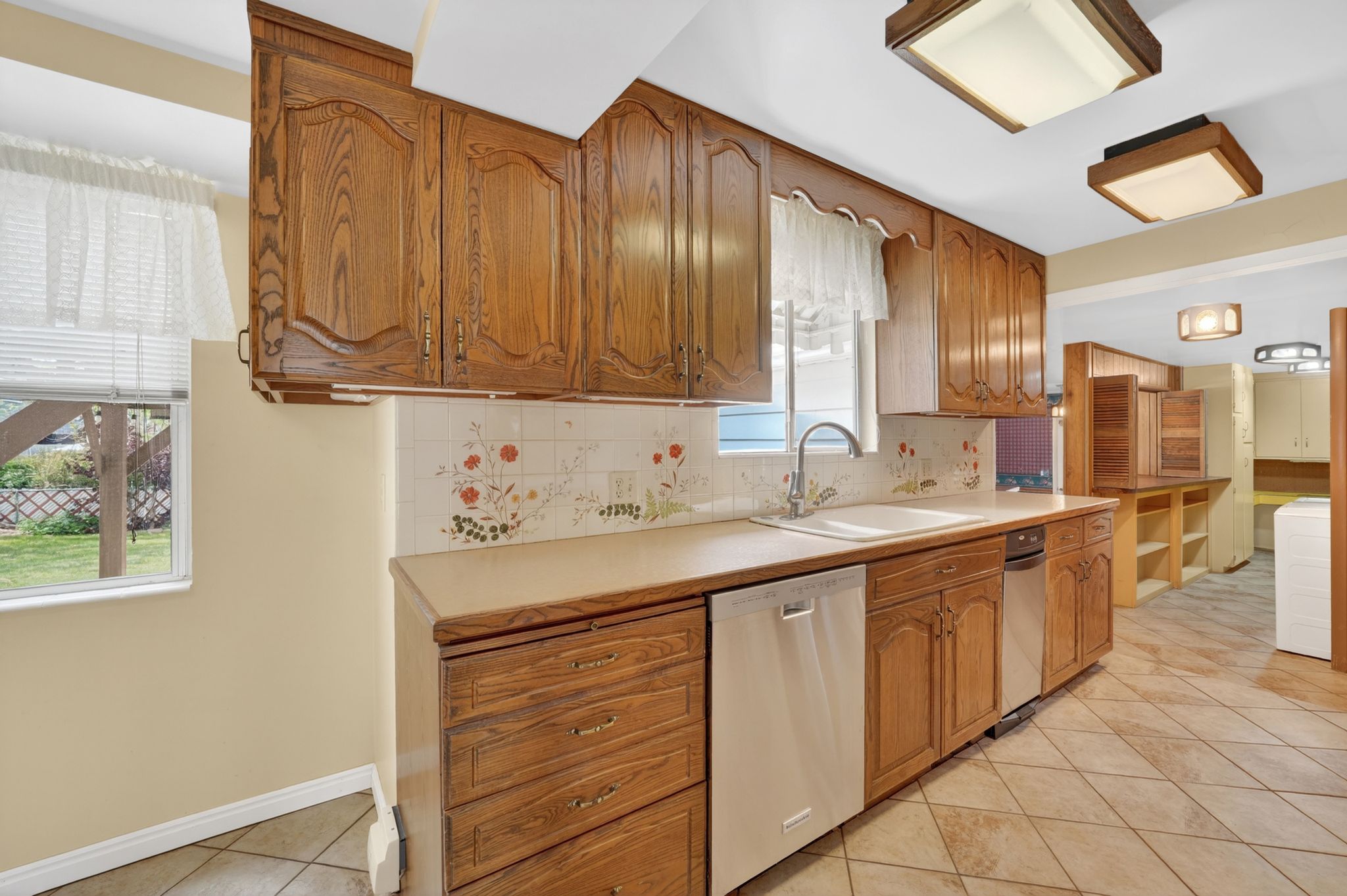 Kitchen featuring ample wood cabinetry, a dual-basin sink, and a white dishwasher